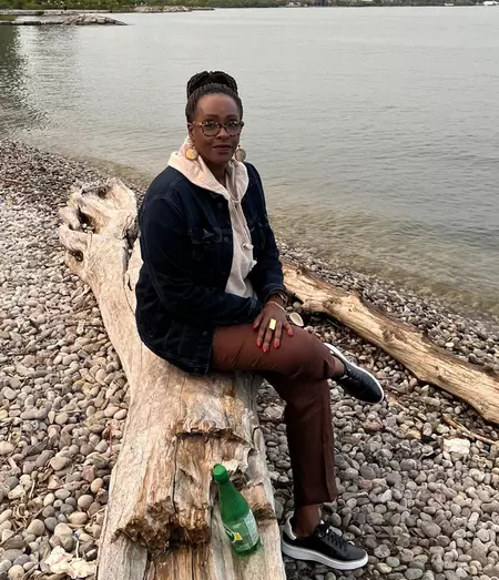 Staff profile photo of Elise Umulisa sitting on a wooden log on a beach.