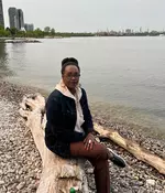 Staff profile photo of Elise Umulisa sitting on a wooden log on a beach.