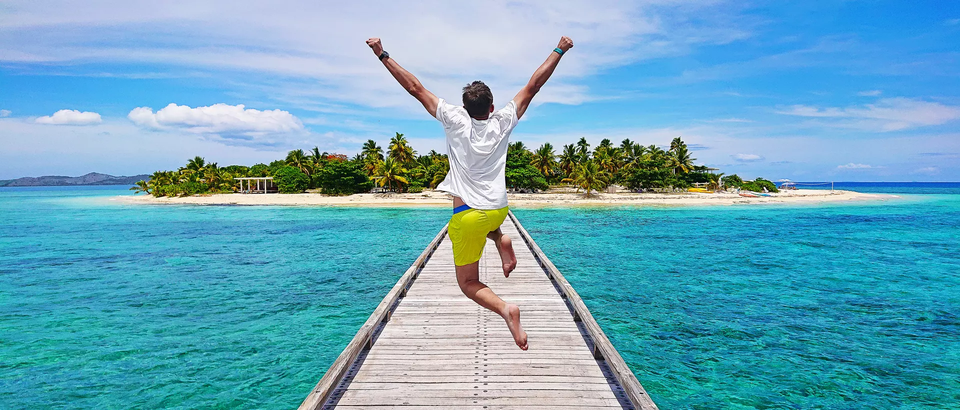 A young traveller jumping with joy on the pier on Mala Mala Island, Fiji.
