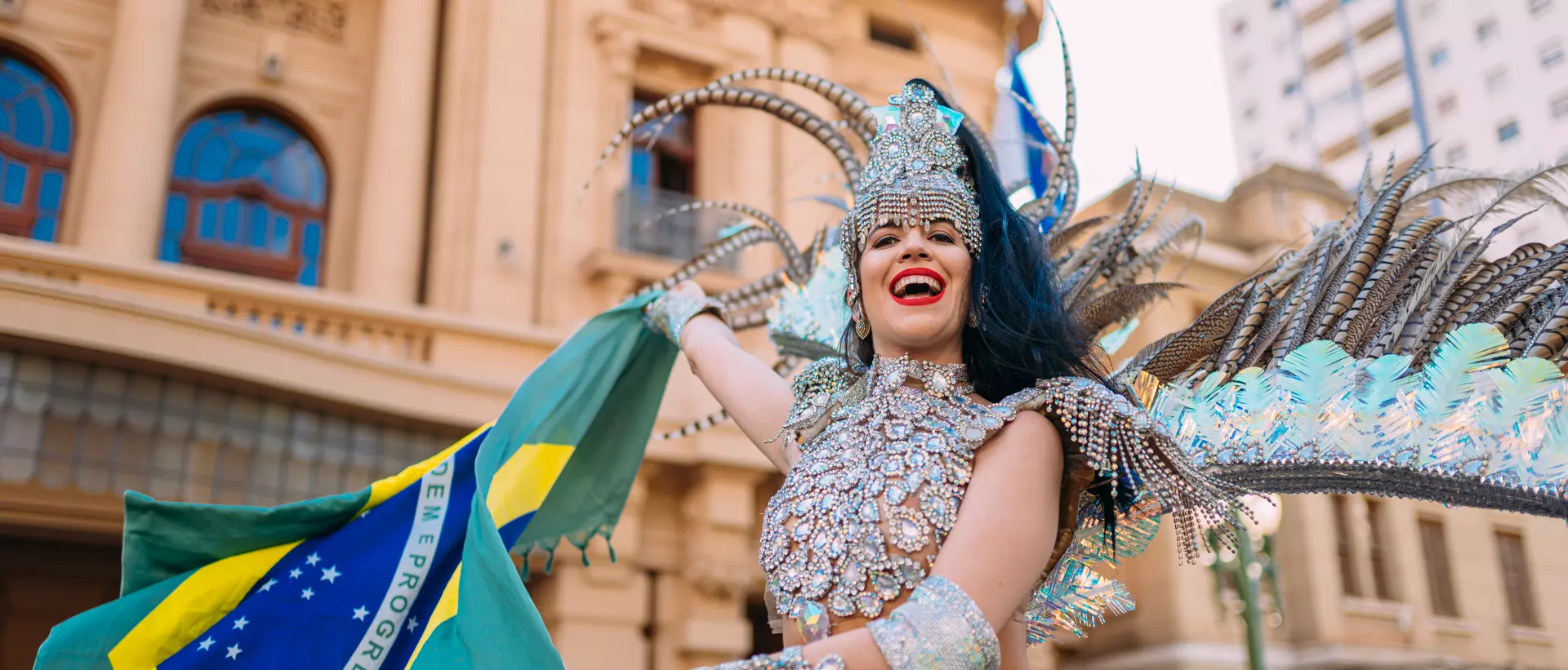 Beautiful Brazilian woman wearing colorful Carnival costume and Brazil flag during Carnaval street parade in city.