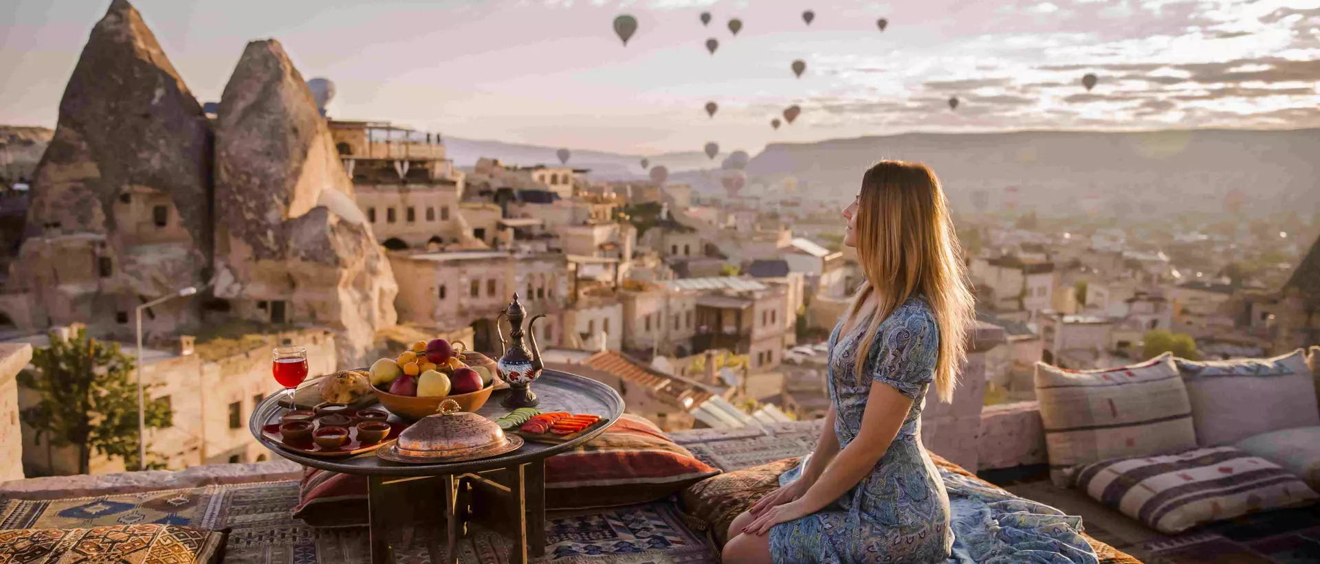 A woman sits on a rooftop in Cappadocia in the early morning sunrise in Turkey
