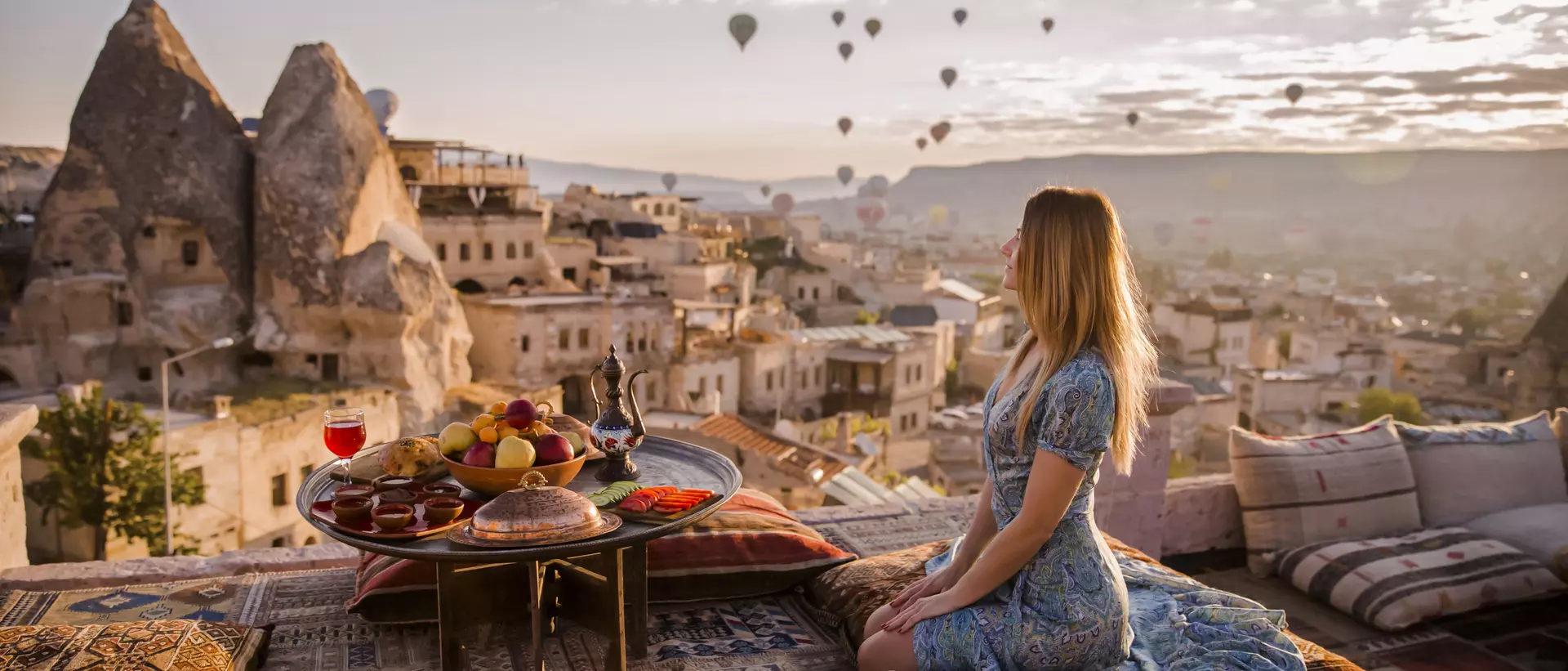 A woman sits on a rooftop in Cappadocia in the early morning sunrise in Turkey