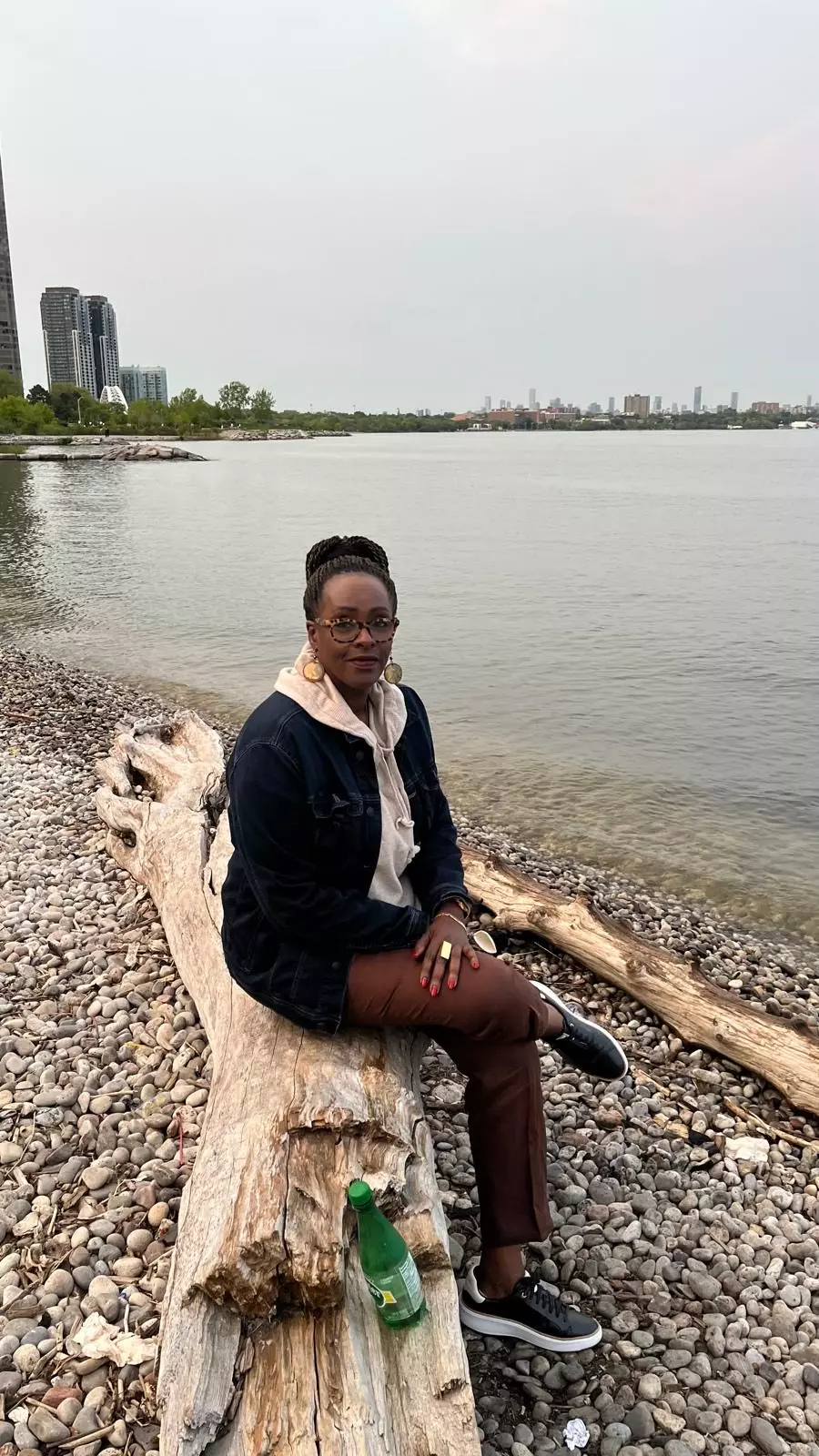 Staff profile photo of Elise Umulisa sitting on a wooden log on a beach.