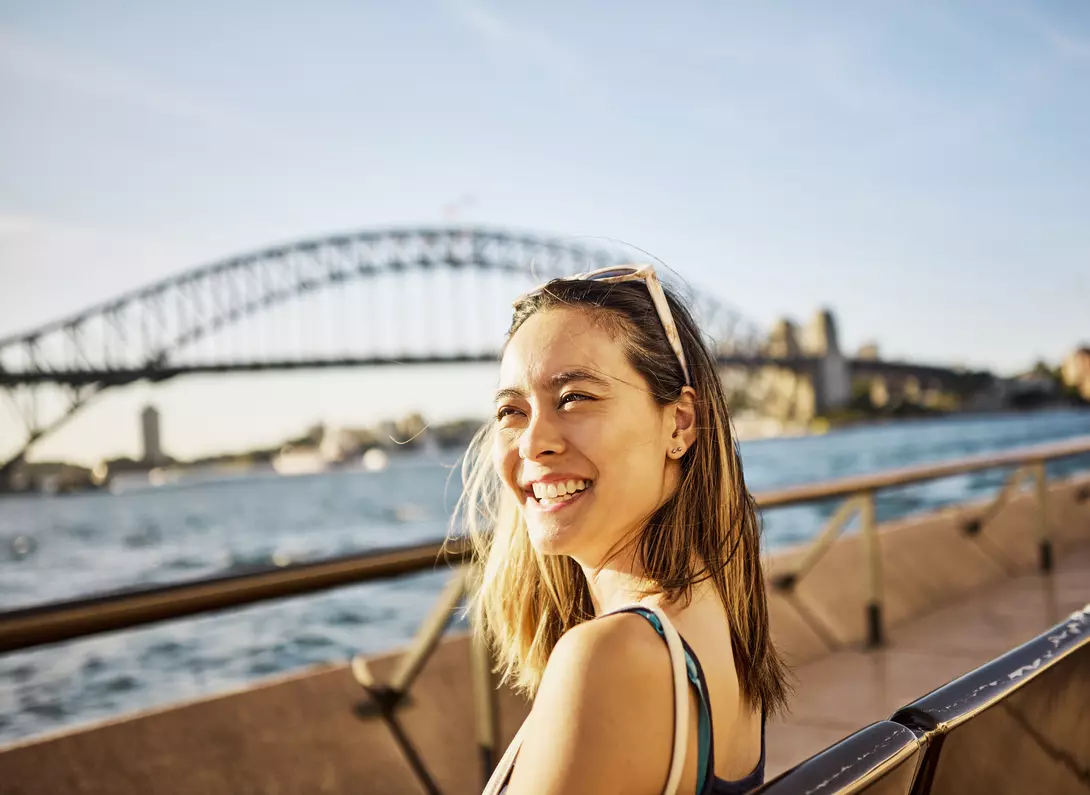 A woman smiles while standing in front of Sydney Harbour Bridge in Australia