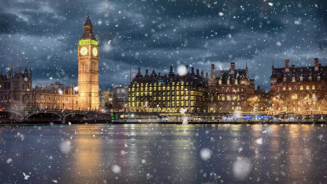 London, England View over the Thames River in London with Big Ben in the background at night during the winter with snow falling.