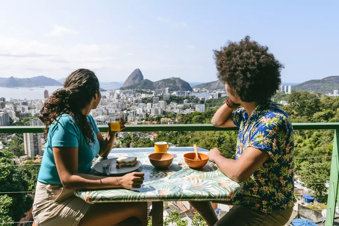 A couple on holiday enjoying a meal in Rio de Janeiro, Brazil, overlooking Sugarloaf mountain from an outdoor rooftop cafe.