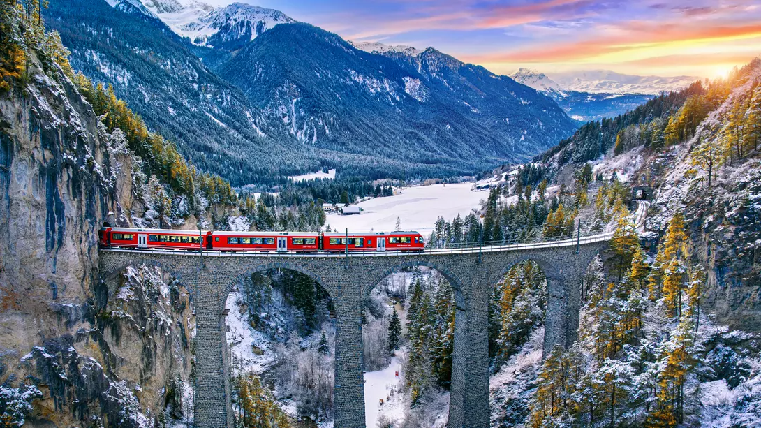 Aerial view of a red train on the elevated Landwasser Viaduct between the famous mountains in Filisur, Switzerland, in a sunny, winter afternoon..