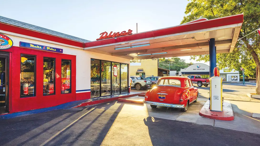 A vintage car at a gas station next to an old diner in middle America