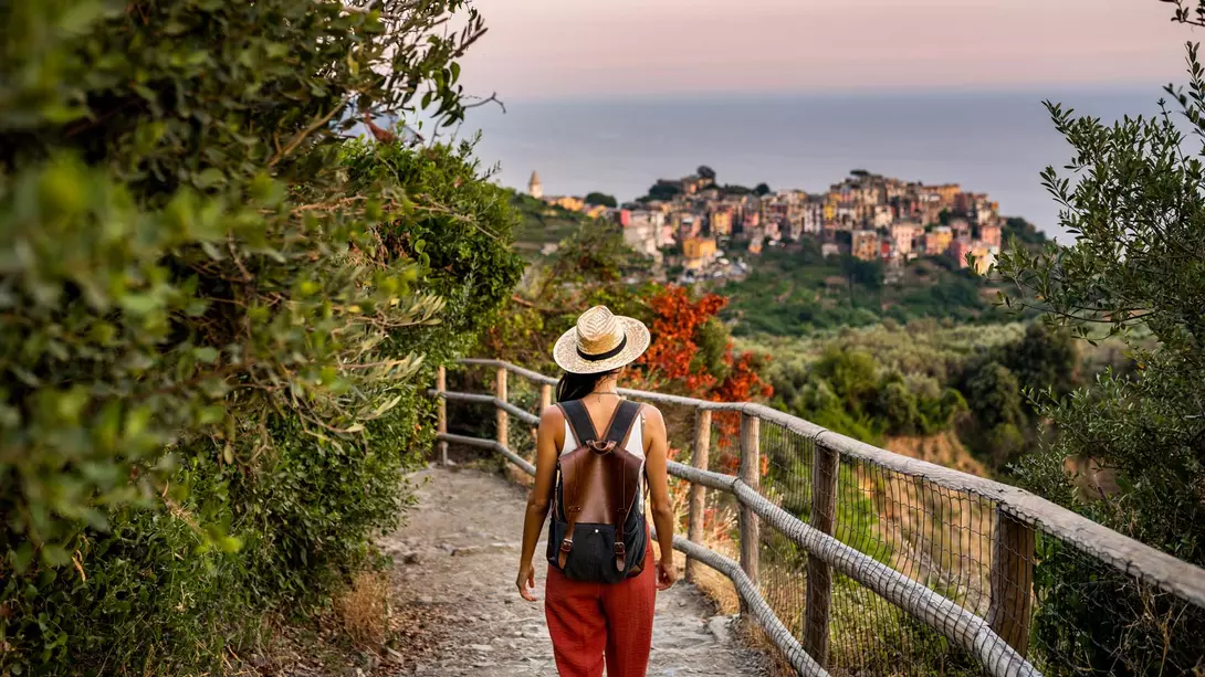 A woman with a hat walks down a hillside path near the coastal village of Corniglia in the Cinque Terre in Italy