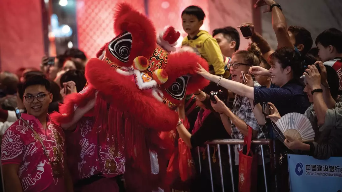Crowds celebrate at a festival with a vivid red lion dance costume and festive atmosphere.