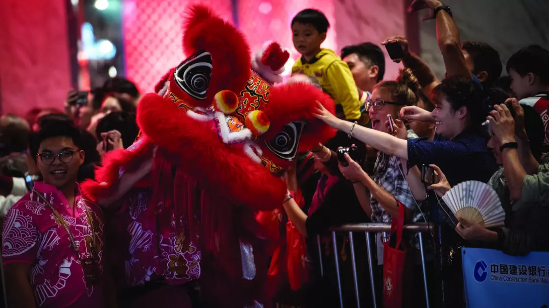 Crowds celebrate at a festival with a vivid red lion dance costume and festive atmosphere.