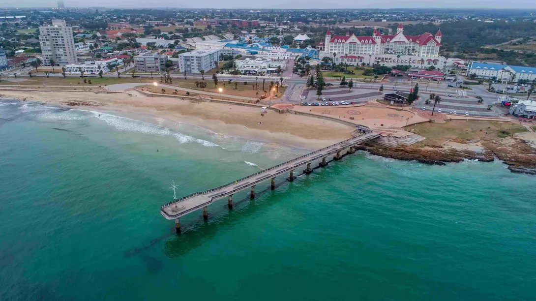 Aerial view of Shark Rock Pier in Port Elizabeth, South Africa. The pier juts out into Algoa Bay, with the city skyline in the background.