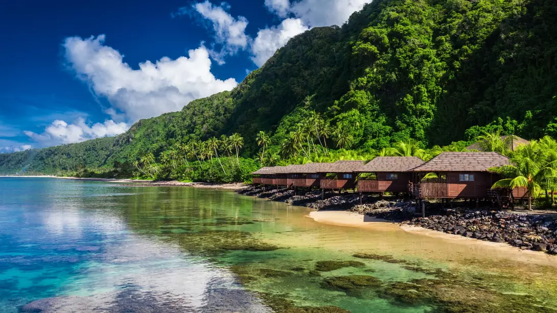 Small beach houses line the shore with green vegetation behind them