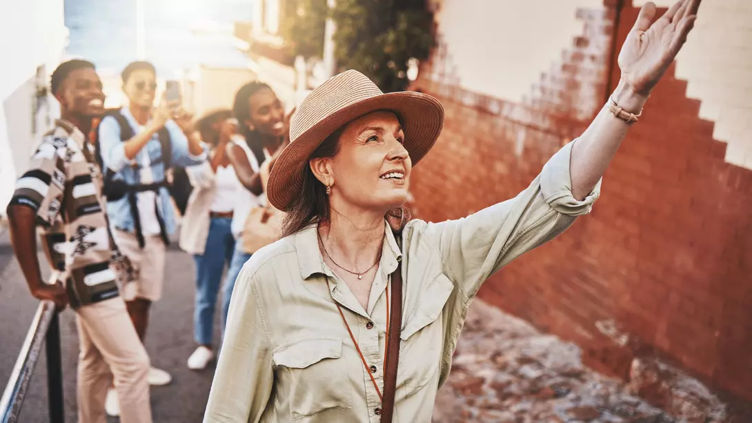 Woman, city guide and group of happy tourists, pointing at local architecture