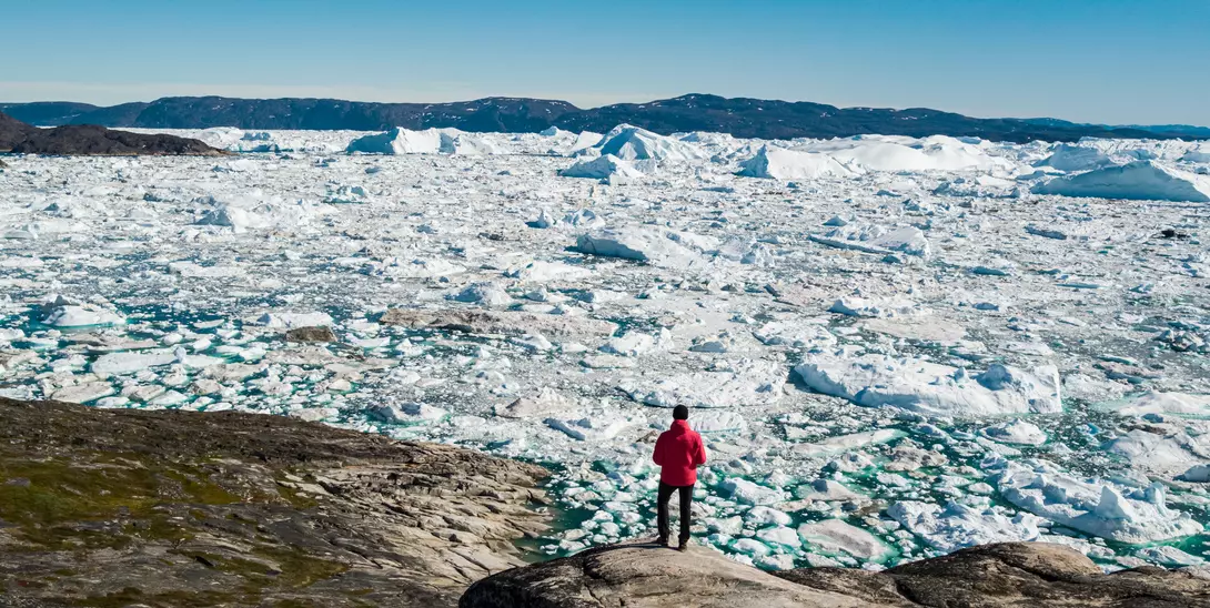 Ilulissat is known for its iceberg flows, which calve off the nearby glaciers. A man stands on the edge of the water watching icebergs in the waters off the town of Ilulissat in central Greenland.