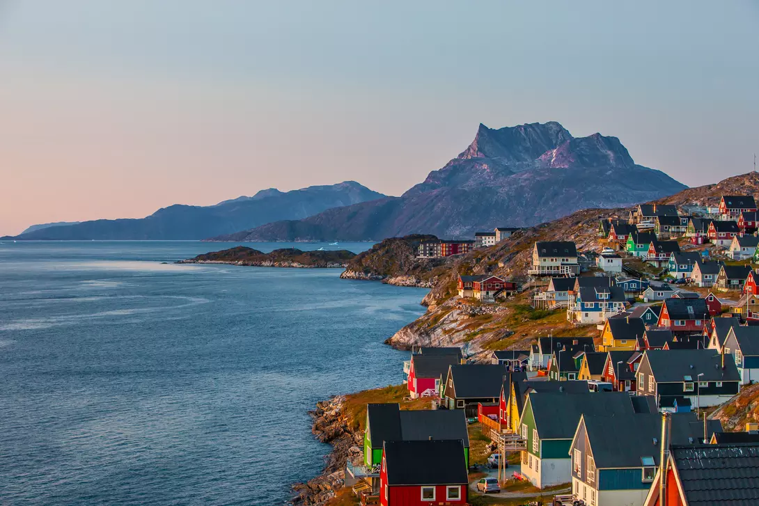 A coastal view of the Greenlandic capital of Nuuk with its colourful homes lining the edge of the water and backdrop of mountains.