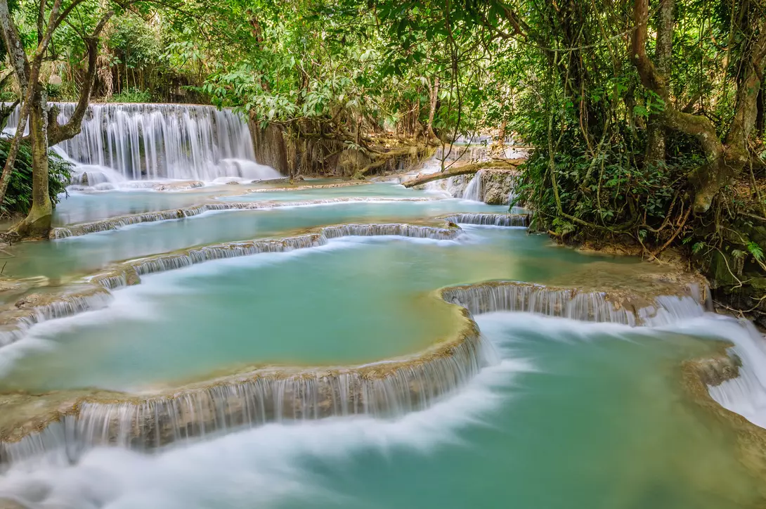 The Kuang Si Falls begin in shallow pools atop a steep hillside. The water flows in to a turquoise blue pool