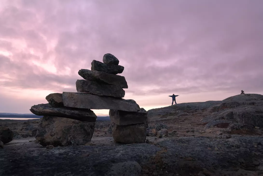 Several inukshuks and a woman becoming one in a beautiful arctic sunset.