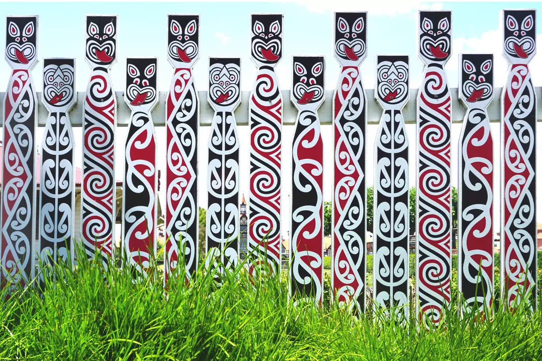 A row of decorated totem poles with intricate tribal patterns in black, red, and white, set against green grass.