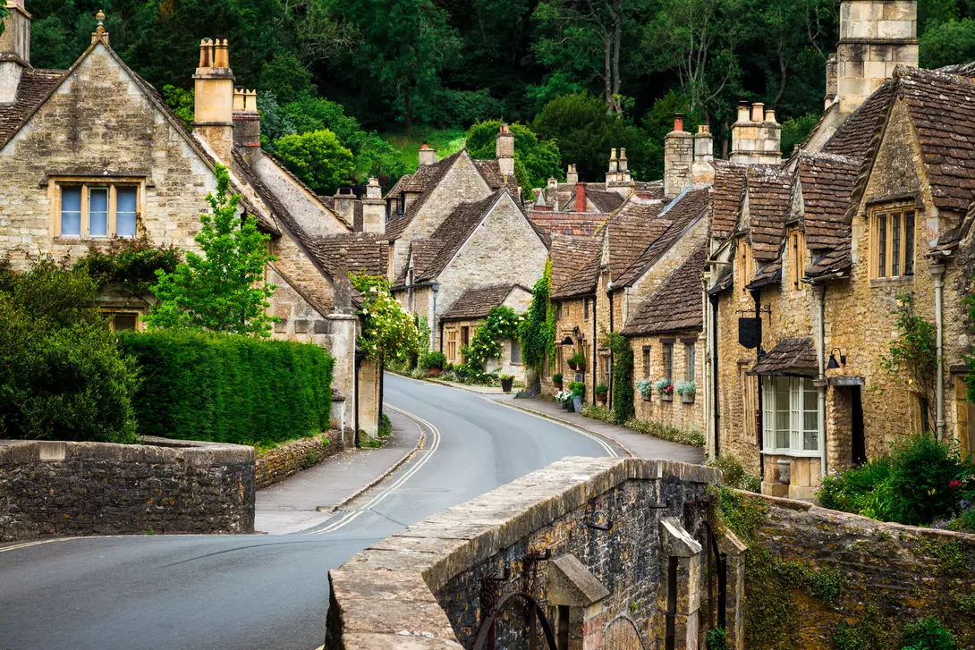 Traditional English village in the Cotswolds area of southwest England. The cosy little brick cottages line the narrow road, and there is also a quaint bridge spanning a little stream.