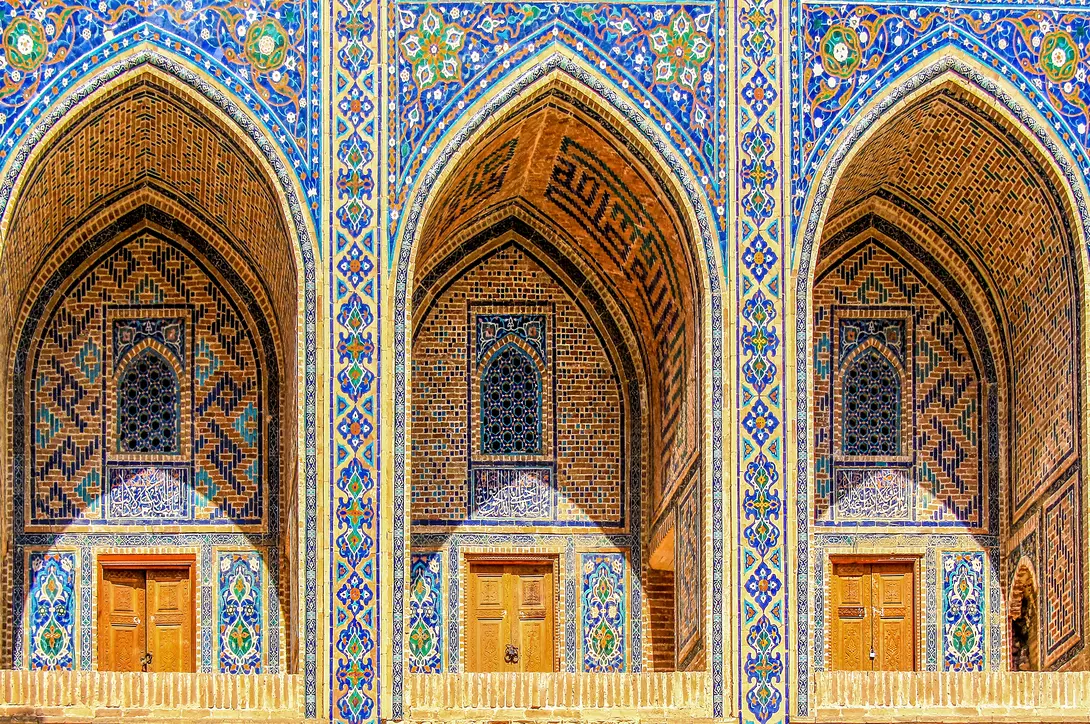Sherdor Madrassah facade with blue, yellow and green tiles, wall with tall arches and windows