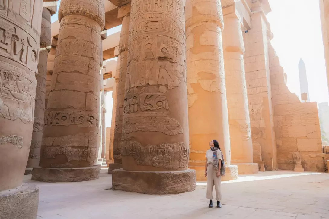 A tourist stands in front of massive carved columns in an Egyptian temple