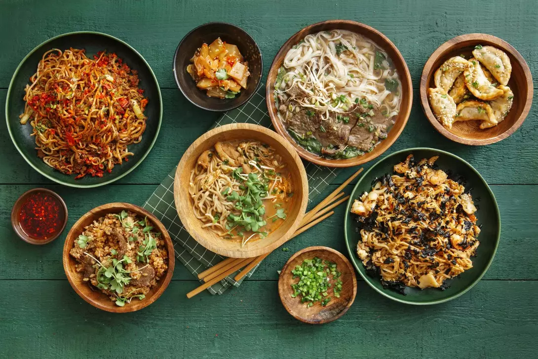 A spread of various Asian dishes including noodles, dumplings, and stir-fried vegetables on a green table.