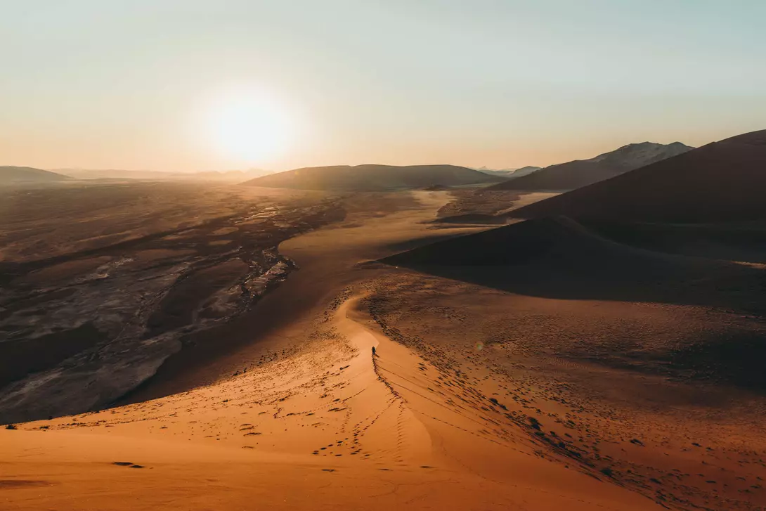 Silhouette of a man walking on the top of the big dune enjoying the dramatic bright desert sunset at Anmib-Naukluft National park