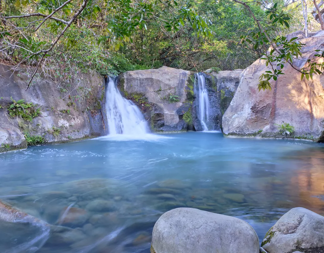 Beautiful blue logoon are surrounded by volcanic rock walls and green foliage