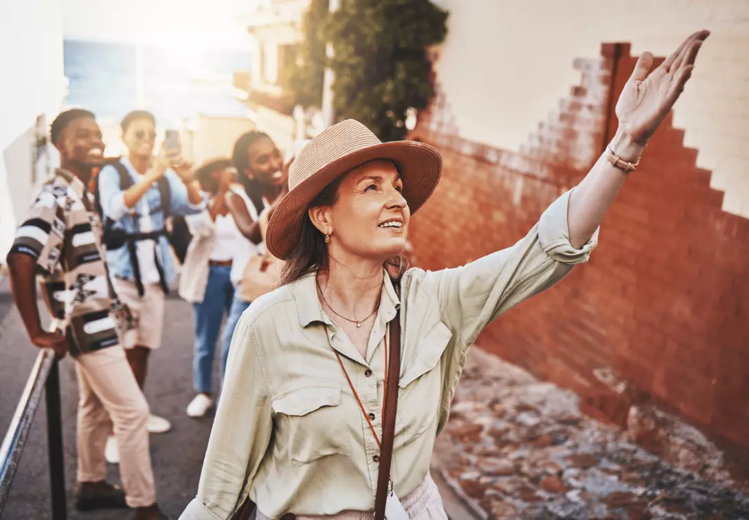 Woman, city guide and group of happy tourists, pointing at local architecture