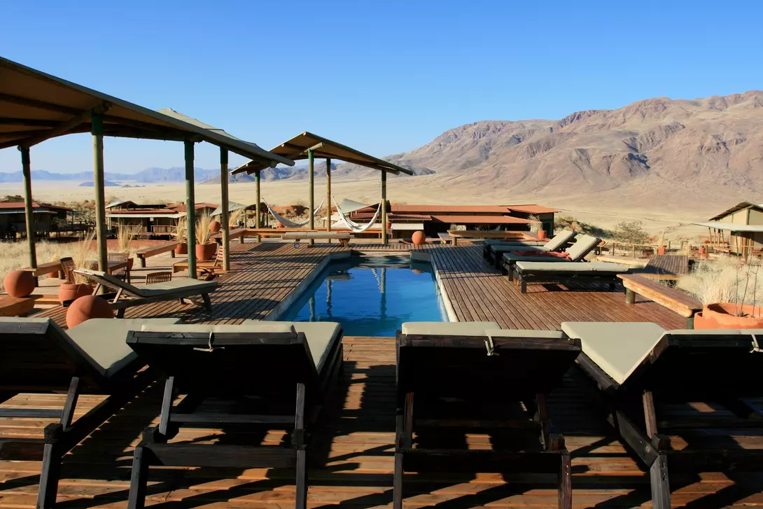 A serene outdoor pool area with lounge chairs, surrounded by mountain views and desert landscape under a clear blue sky.