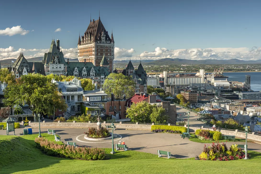 A scenic view of Quebec City featuring the iconic Chateau Frontenac, surrounded by green spaces and colorful flowers.