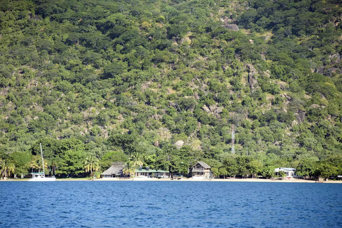 A panoramic view of Lake Malawi, Africa. The lake is surrounded by lush green hills and has crystal-clear blue water.