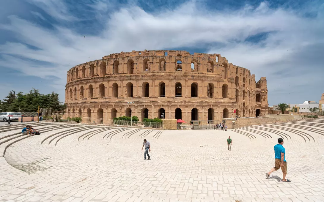 The ancient Roman amphitheater stands tall under a blue sky, surrounded by visitors on a sunny day.