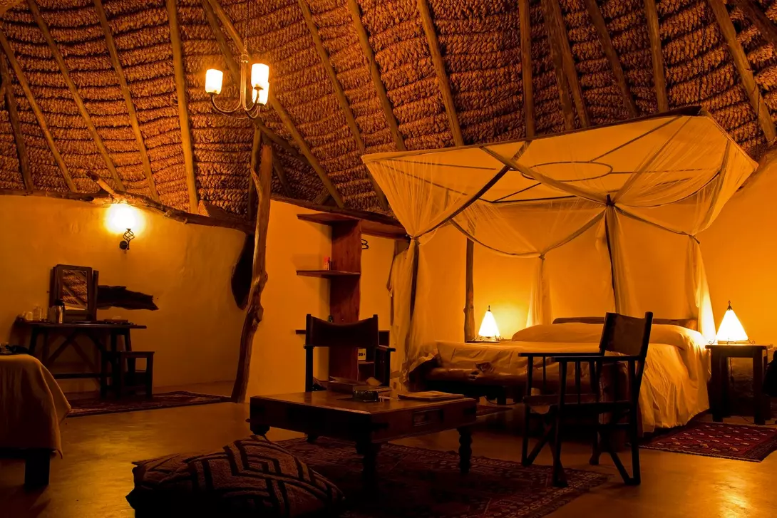 Interior of a cozy, warmly lit room with a thatched roof, featuring a bed with a canopy and rustic furniture.
