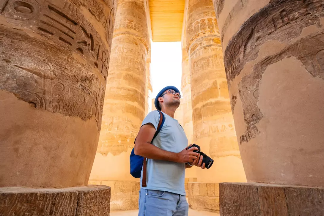 Person standing between ancient stone columns, gazing up, holding a camera
