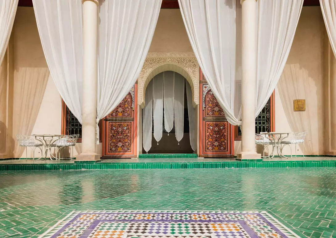 Elegant interior with green tiled floor, sheer drapes, and intricately carved wooden doors in a Moroccan-style setting.