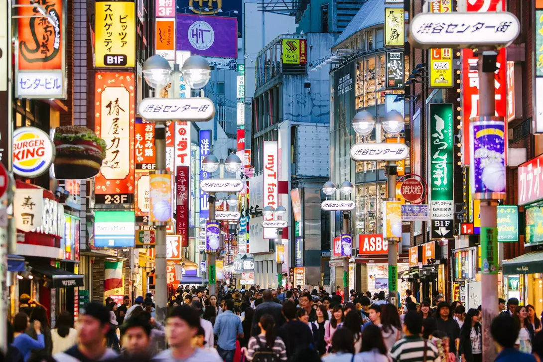 Busy street scene in a city, illuminated by colorful signs and bustling with people.