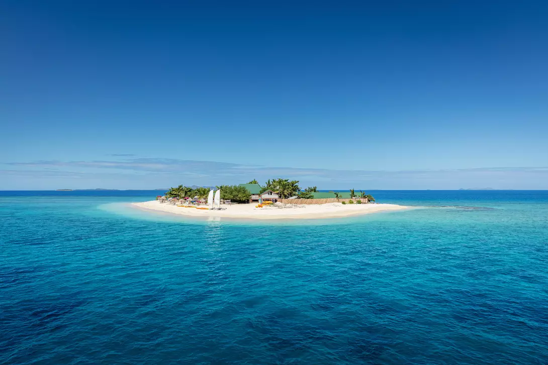 Beautiful small island in the middle of the south pacific ocean with beach huts, lounge chairs, palm trees, surrounded with beautiful clear turquoise water.