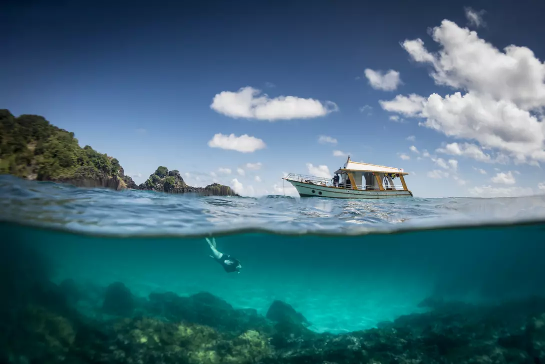 View of a tour boat and a woman free diving at 'Sancho' beach in the archipelago of Fernando de Noronha