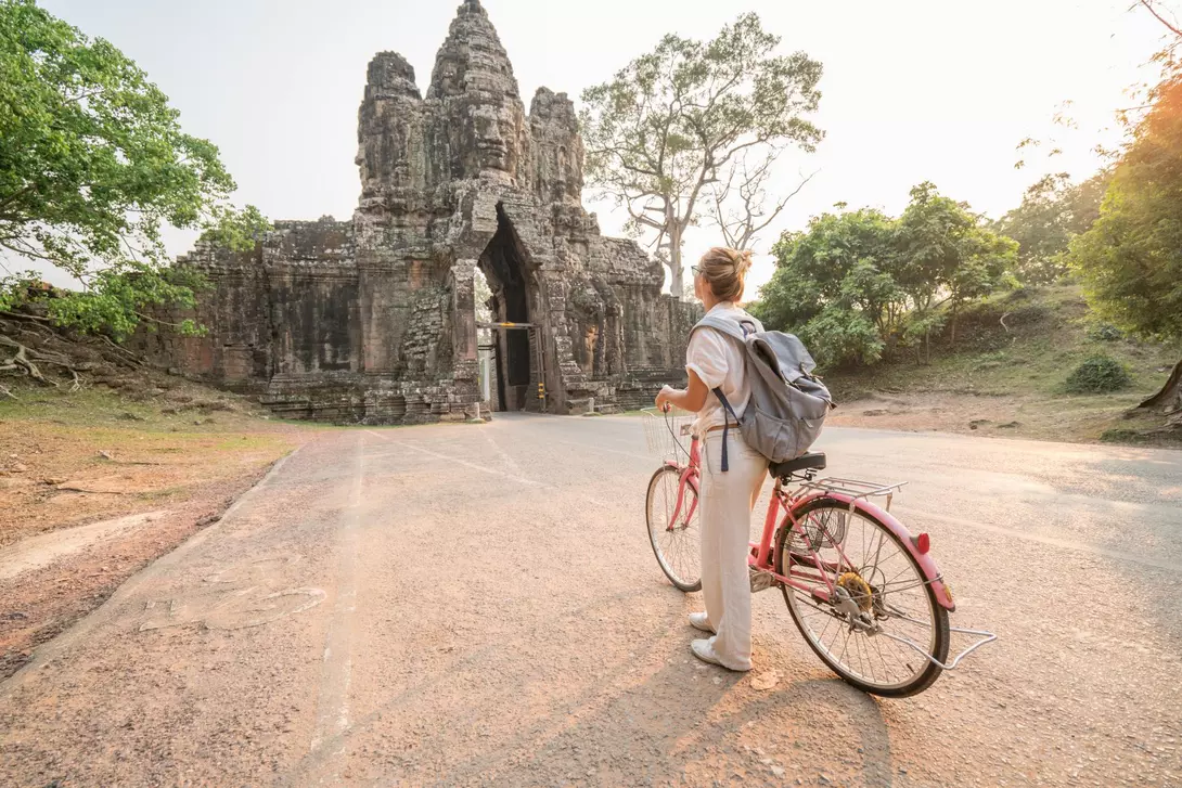 Angkor Wat Young woman traveling in Cambodia visiting the temples of Angkor wat complex by bicycle.