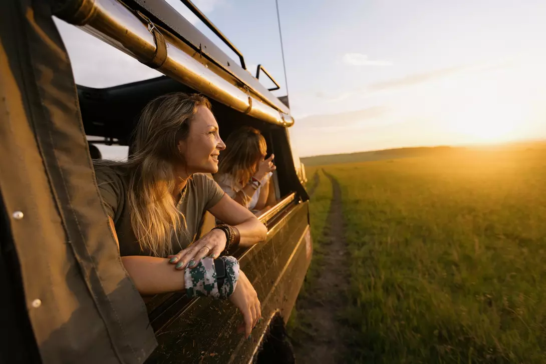 Kenya A woman in a Land Cruiser on a safari game drive at sunset leaning out of the vehicle window.