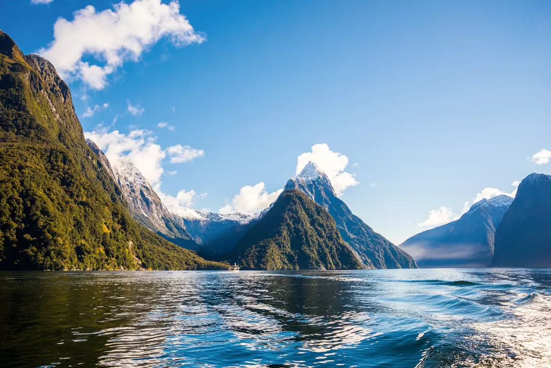 Milford Sound, New Zealand Towering forested peaks, snowy mountains, and calm blue waters under a clear sky in New Zealand’s dramatic Milford Sound fjord.