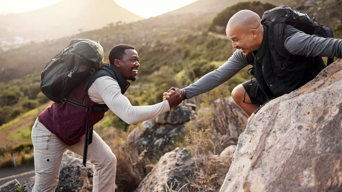 two hikers help each other get over rocks on a mountain