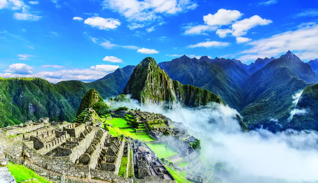 ruins of machu picchu draped in mist with backdrop of mountains