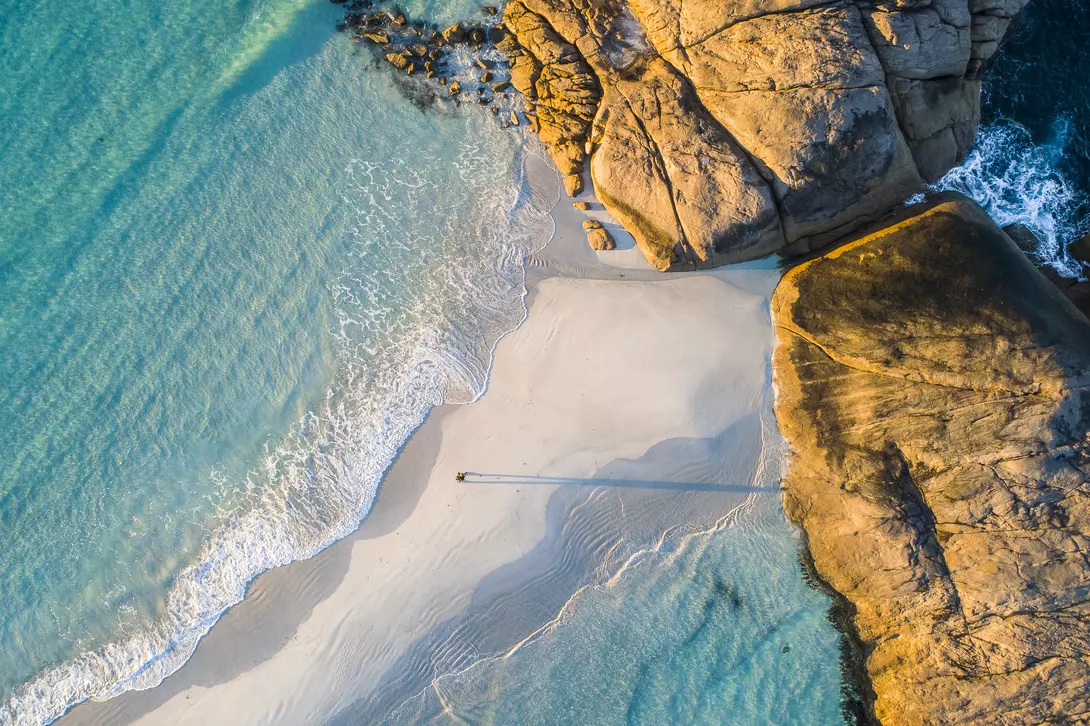 Coastline aerial photograph of aquamarine ocean and man walking along white sandbar beach in Australia