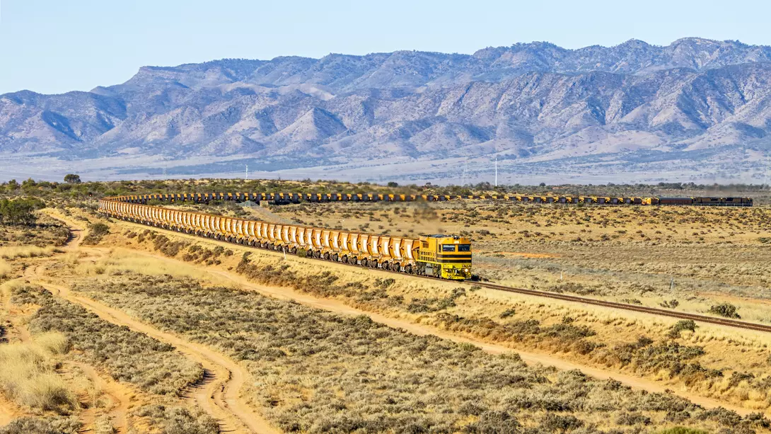 View of long, loaded iron ore train from northern South Australian mine with Flinders Ranges background.