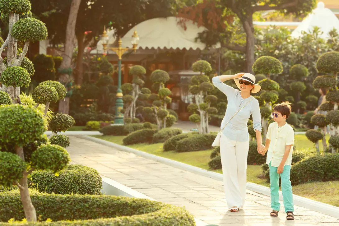 Young mother and her little son walking in Green bonsai trees gardens in Wat Arun, Bangkok, Thailand