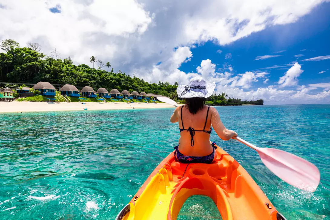 woman kayaking in waters off a beach with bungalows