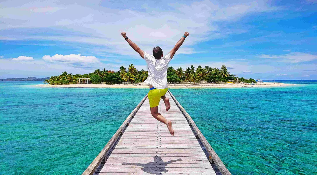 A young traveller jumping with joy on the pier on Mala Mala Island, Fiji.